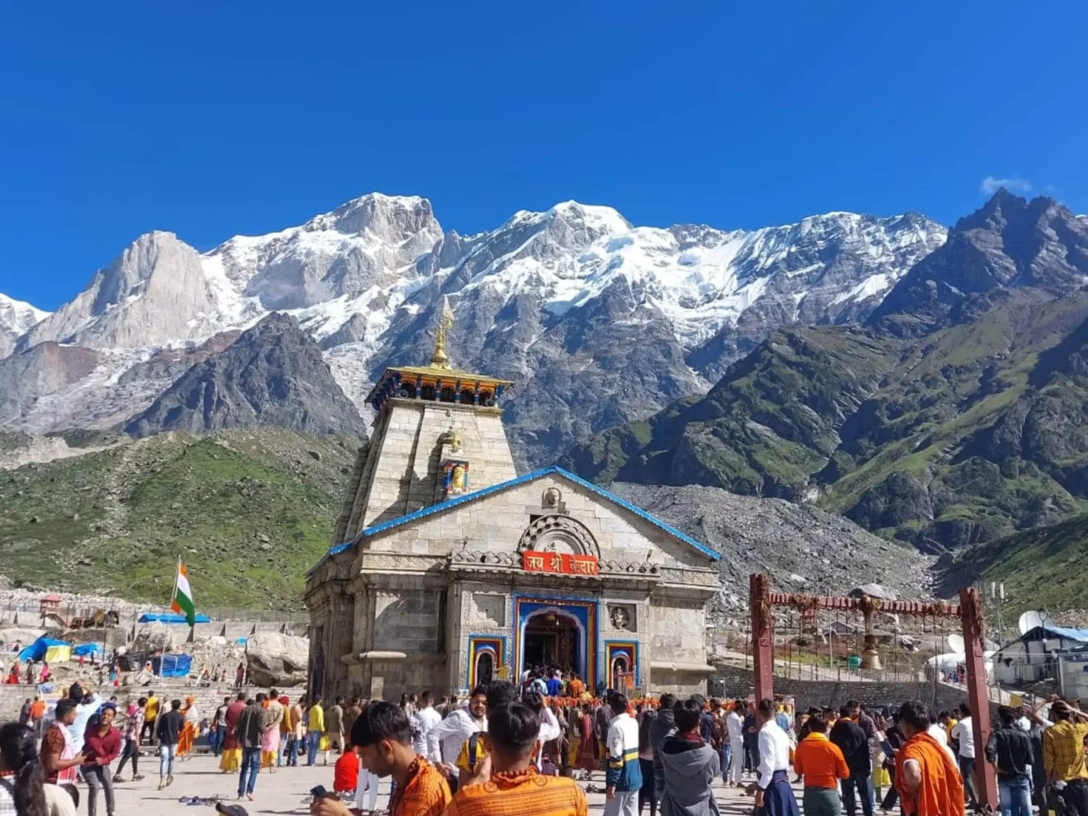 Devotees praying outside Kedarnath Temple under clear blue skies.