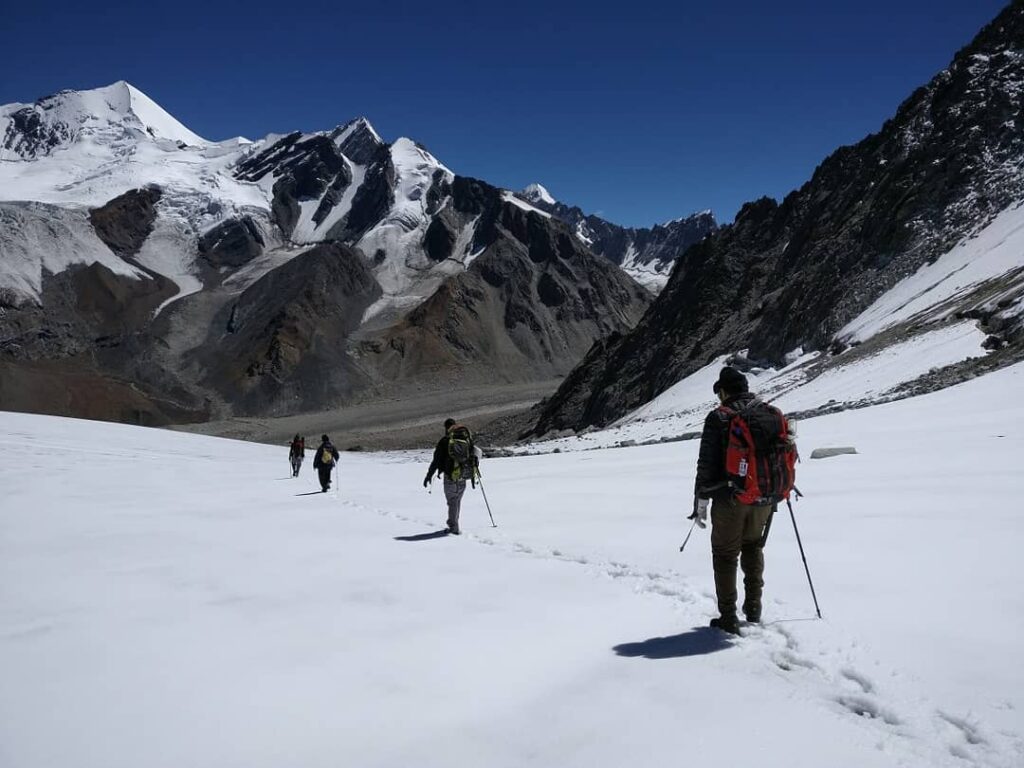 Trekkers navigating thick snow on Borasu Pass trail, one of India’s most difficult treks, with distant Himalayan mountains in view.