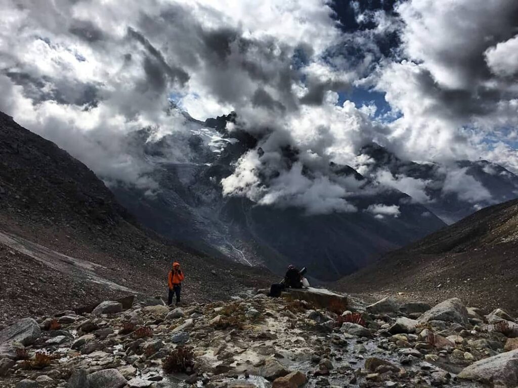 A trekker rests while admiring the dramatic sky over Pin Parvati Pass, one of the most difficult and scenic treks in India.