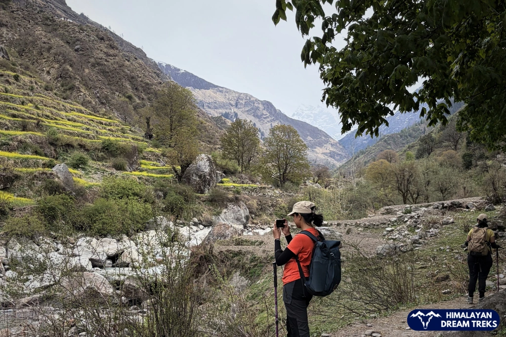 A female trekker taking a photograph while standing on a mountain trail