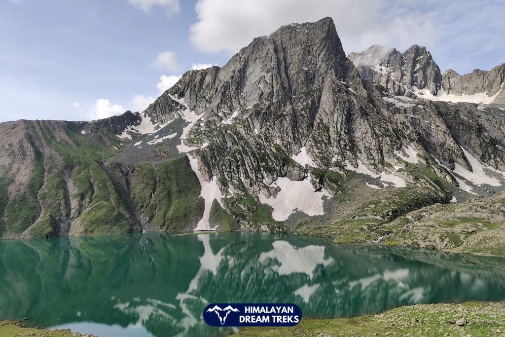 Gadsar Lake with green water and rocky snow-covered mountains in Kashmir Great Lakes Trek