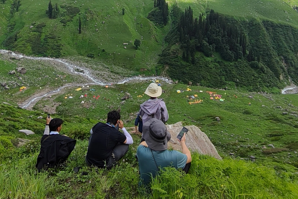 Trekkers resting on a ridge, overlooking a peaceful green valley